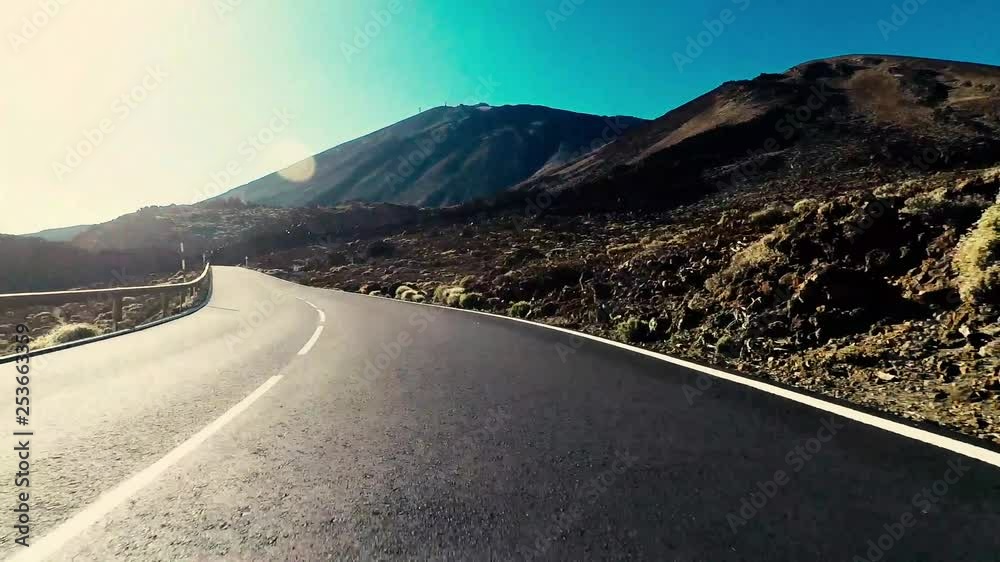 Long way road at the mountain with sun in front and sunlight effect - ground point of view with black asphalt and white lines - driving and travel concept