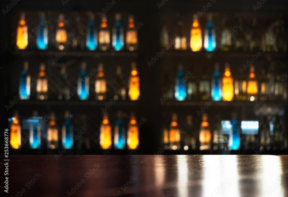 top of wood table with neon orange blue light of alcohol bottle in dark bar and club background