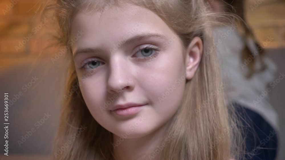 Close-up portrait of small pretty caucasian girl adjusting her hair and watching calmly into camera in cosy home atmosphere. Close-up portrait of small pretty caucasian girl adjusting her hair and watching calmly into camera in cosy home atmosphere.