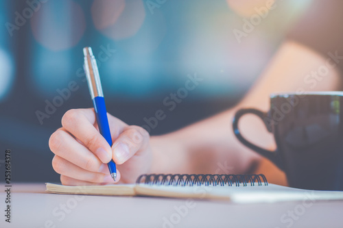 Business woman s hand is writing on a notebook with a pen.