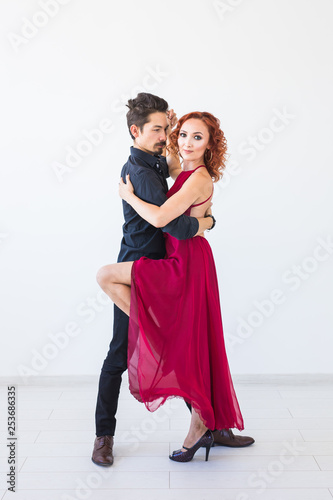 Social dance, bachata, kizomba, salsa, tango concept - Woman dressed in red dress and man in a black costume over white background