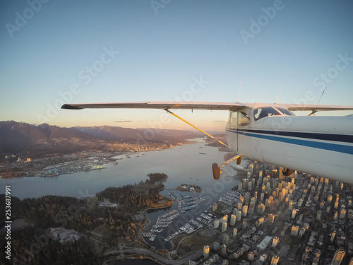 Small airplane flying over Downtown City during a vibrant sunset. Taken in Vancouver, British Columbia, Canada.