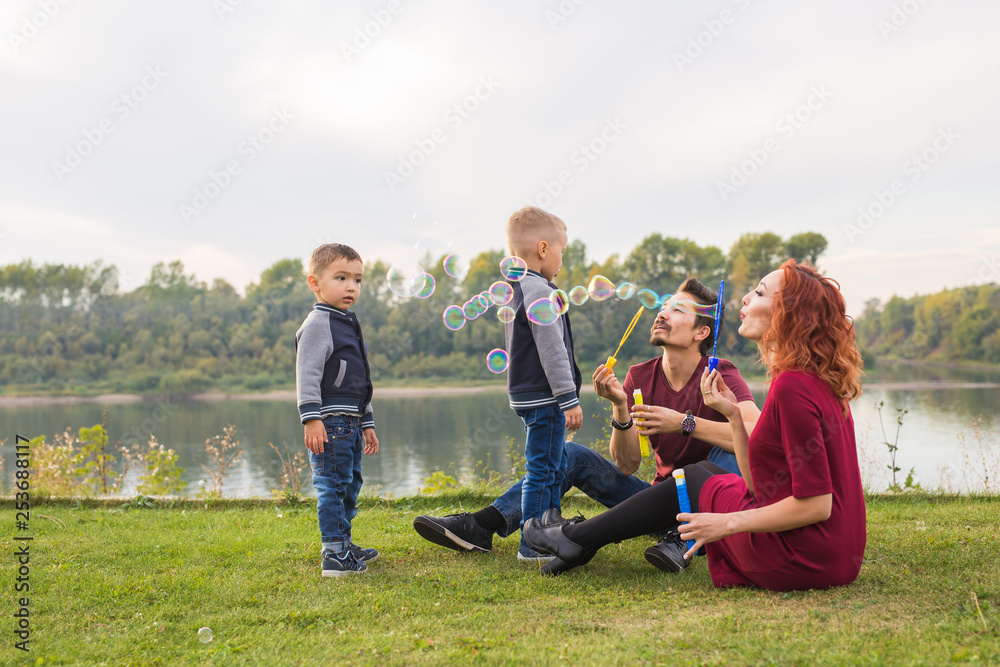 Family and nature concept - Mother, father and their children playing with colorful soap bubbles Family and nature concept - Mother, father and their children playing with colorful soap bubbles