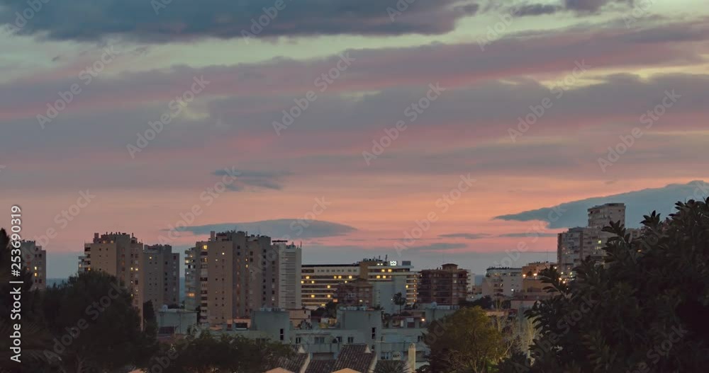 Slow zoom timelapse of red and pink clouds moving fast during sunset over a view of apartment buildings and hotels in Costa Del Sol, Spain. Lots of windows lighting up. Slow zoom timelapse of red and pink clouds moving fast during sunset over a view of apartment buildings and hotels in Costa Del Sol, Spain. Lots of windows lighting up.