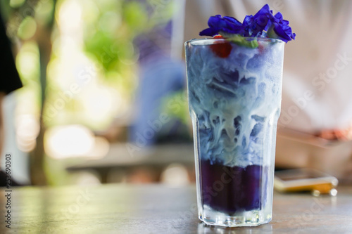 A glass of butterfly pea flower latte iced drink with blur interior cafe background