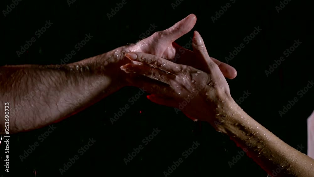 close-up view of wet hands of man and woman under flows of water in black background close-up view of wet hands of man and woman under flows of water in black background