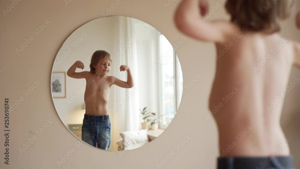 Confident kid looking at his muscles in mirror imagining that he is super hero