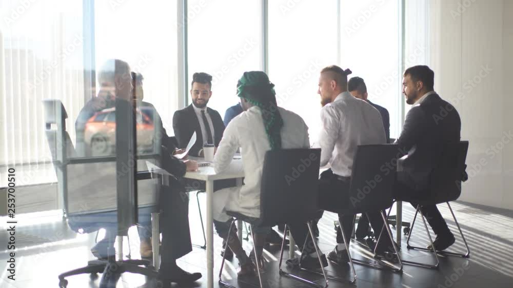 Multiracial team of business partners of different age interacting in boardroom of modern spacious and well-lit office, being viewed through transparent glass wall. Multiracial team of business partners of different age interacting in boardroom of modern spacious and well-lit office, being viewed through transparent glass wall.