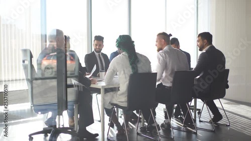 Multiracial team of business partners of different age interacting in boardroom of modern spacious and well-lit office, being viewed through transparent glass wall.