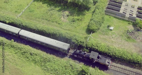 Overhead aerial view of a steam locomotive pulling carriages over a level crossing into Bodiam train station, East Sussex, England. photo