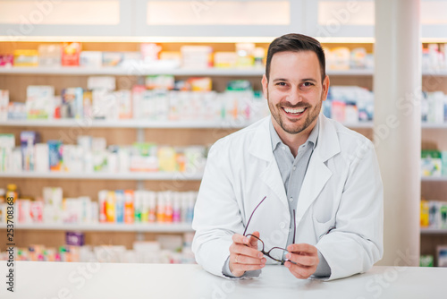 Portrait of a cheerful handsome pharmacist leaning on counter at drugstore. photo