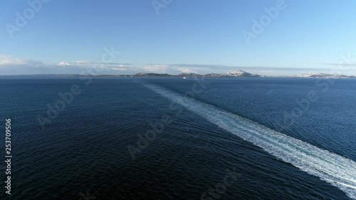 Aerial footage of flying past a ferry sailing forward with snowy mountains in the background. photo