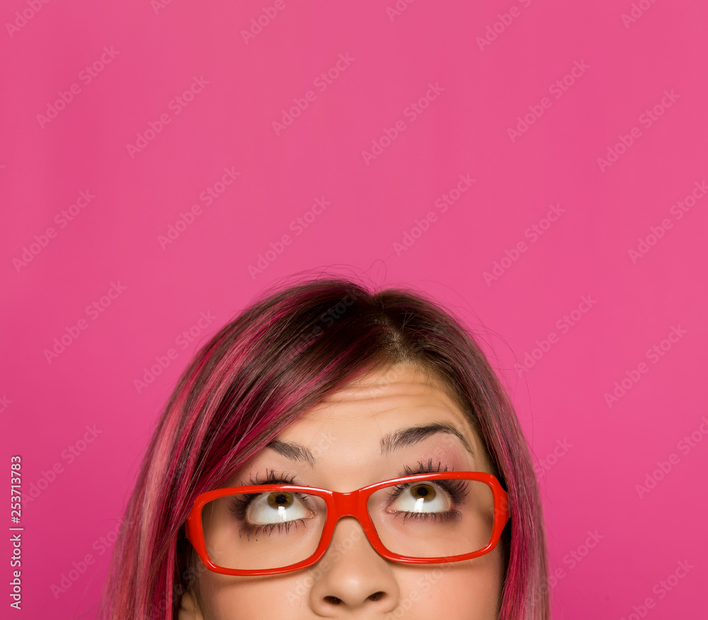 Half portrait of a young worried woman with pink hair and glasses on pink background