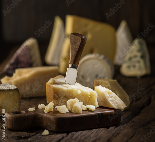 Piece of Parmesan cheese  on the wooden board. Assortment of different cheeses at the background.