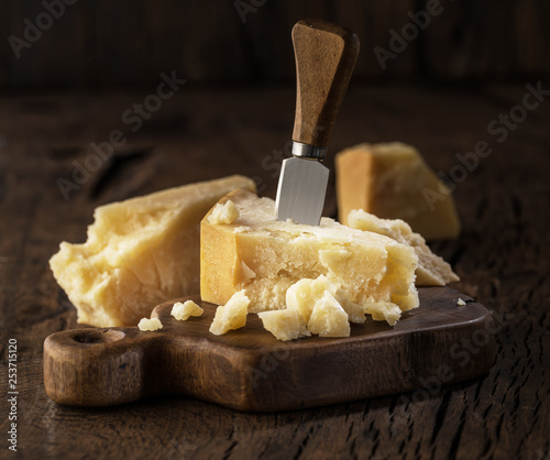 Piece of Parmesan cheese and cheese knife on the wooden board. Dark background.