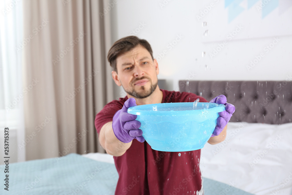 Man collecting leaking water from ceiling in bedroom. Time to call plumber Man collecting leaking water from ceiling in bedroom. Time to call plumber