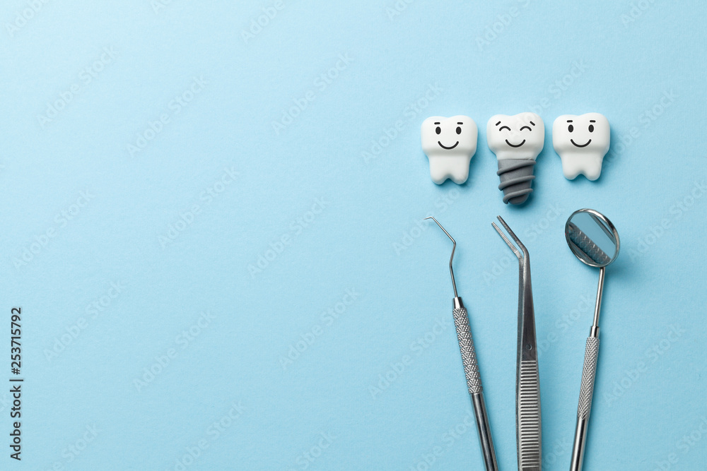 Healthy white teeth and implants are smiling on blue background and dentist tools mirror, hook. Copy space for text. - obrazy, fototapety, plakaty 