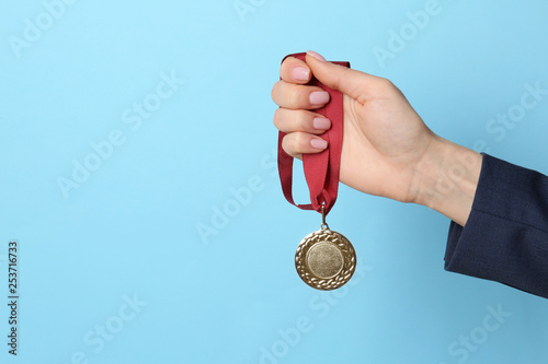 Woman holding golden medal on color background, closeup. Space for text