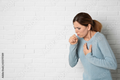 Fototapeta Woman suffering from cough near brick wall. Space for text