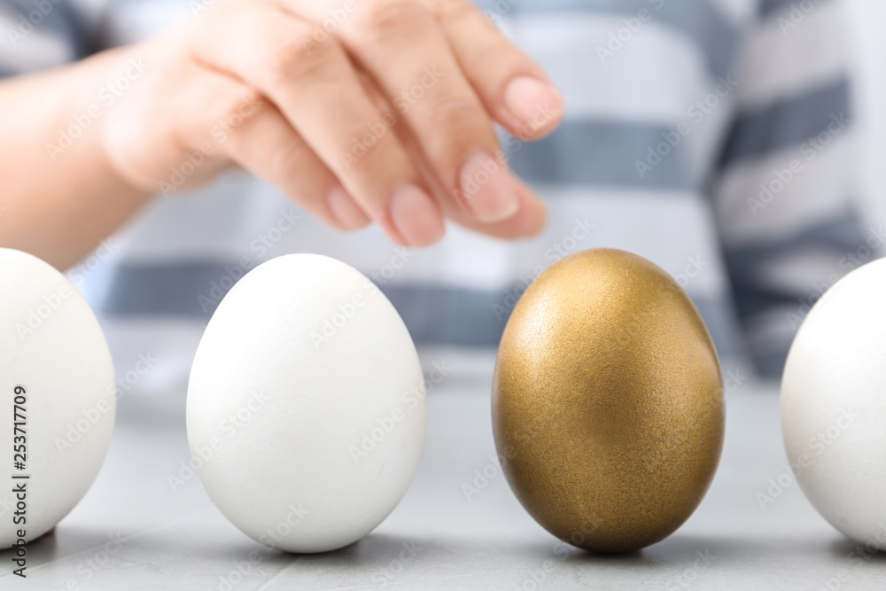 Woman choosing golden egg from white ones at table, closeup - obrazy, fototapety, plakaty 