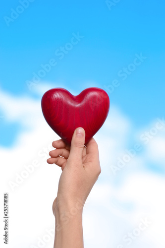 Woman holding decorative heart in hand on color background, closeup
