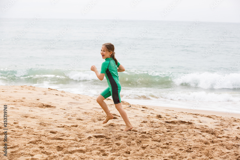 Girl running on tropical beach, having fun, smiling, dressed in protective wetsuit.
