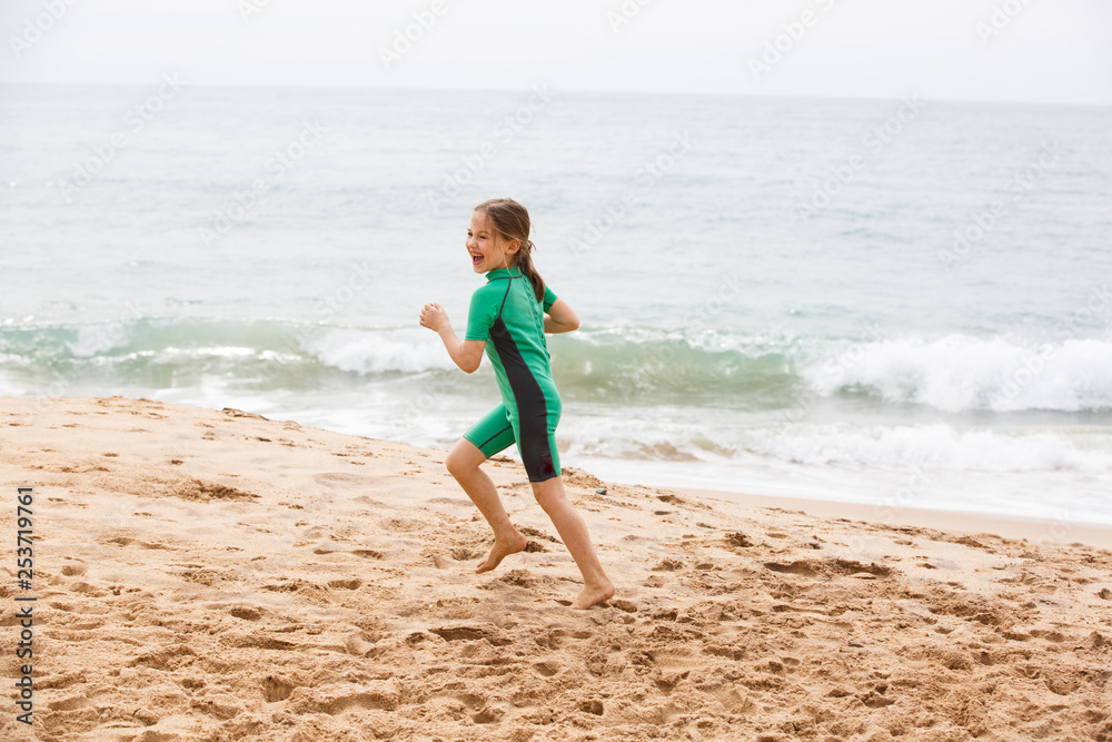 Girl running on tropical beach, having fun, smiling, dressed in protective wetsuit. Girl running on tropical beach, having fun, smiling, dressed in protective wetsuit.