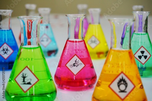 Many of Erlenmeyer flask with colorful solution and Variety type of chemical hazard warning symbols labels. Focus on Explosive sign,symbol. photo