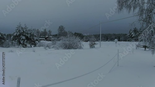 Flying pass a pine tree, almost thrue it. its covered with snow and out on a field and you can see an Electric fence and a Electric wire and trees photo