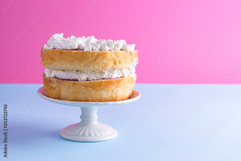 A festive sponge cake with white cream for a birthday, on a pink and blue background. Food for the holiday. Advertising poster and place for text. Copy cpace. фотография Stock
