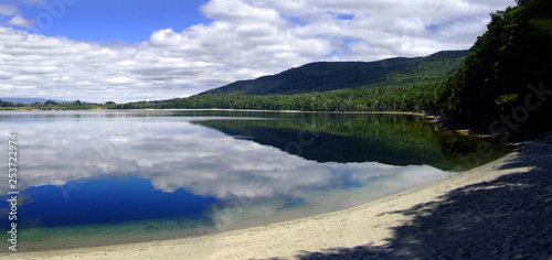 Lake Te Anau surface reflecting white clouds with blue sky and sandy beach. South island, New Zealand Kepler track