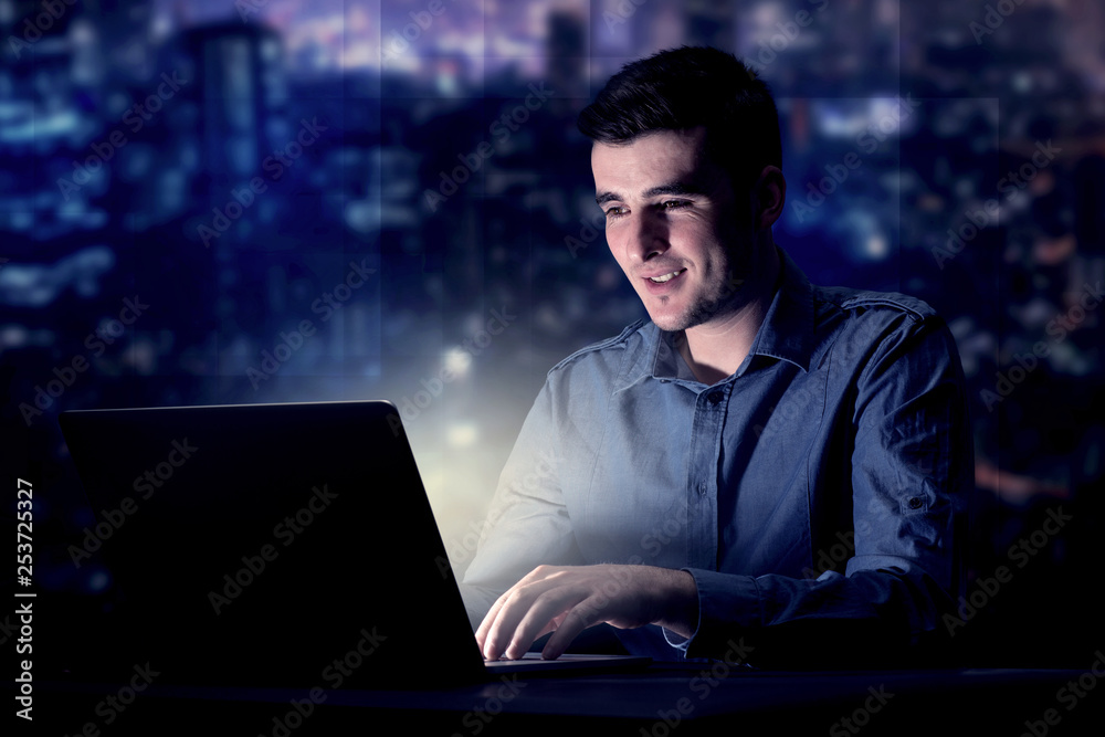 Young handsome businessman working late at night in the office with blue lights in the background Young handsome businessman working late at night in the office with blue lights in the background