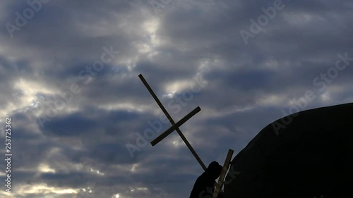 man in hoodie lifting Christian cross up to rock top slow motion silhouette photo