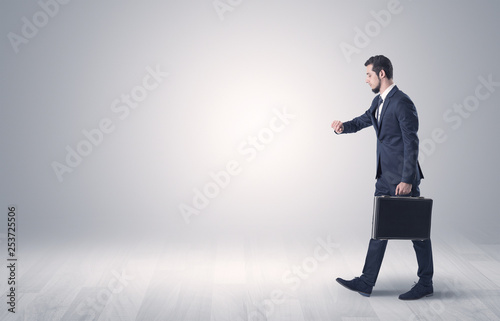 Successful businessman walking in front of an empty wall with briefcase on his hand 