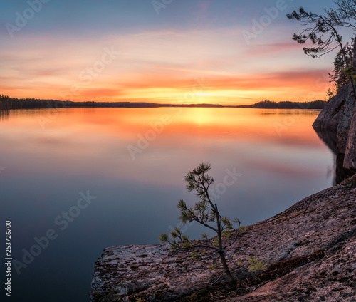 Scenic sunset landscape with peaceful lake and tree at summer evening in Finland