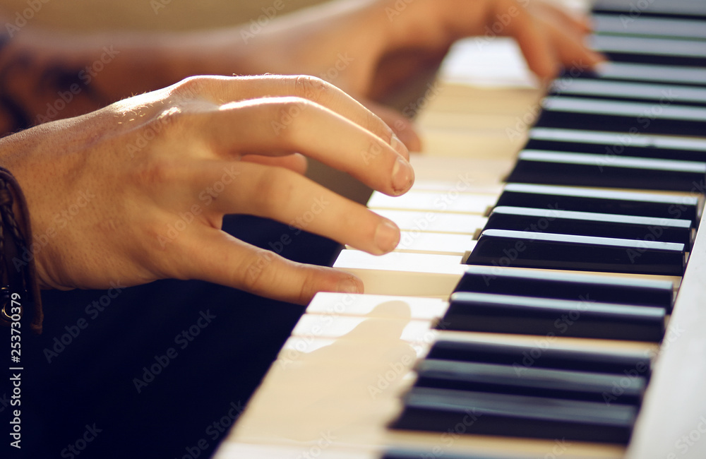 On a musical keyboard instrument, which is illuminated by the sun, a man plays a melody with his hands. On hand to wear the bracelet.