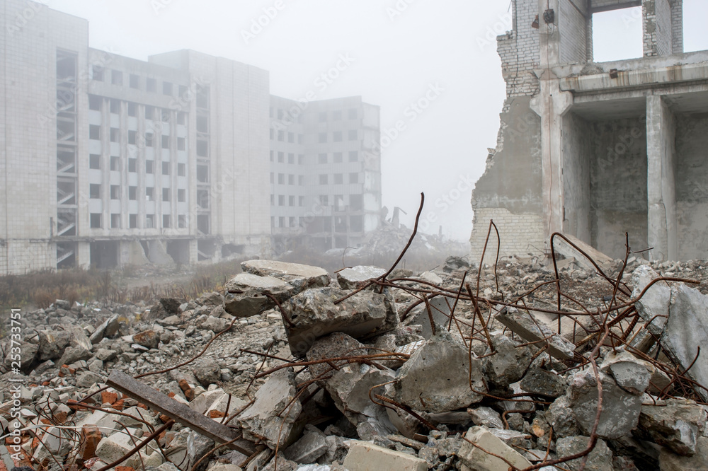 Fragments of concrete stones with protruding reinforcement on the background of the building in a foggy haze. Background - obrazy, fototapety, plakaty 