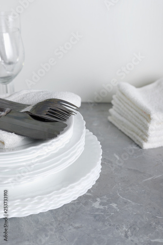 Stack of clean plates with forks, knives and glasses for serving on stone table