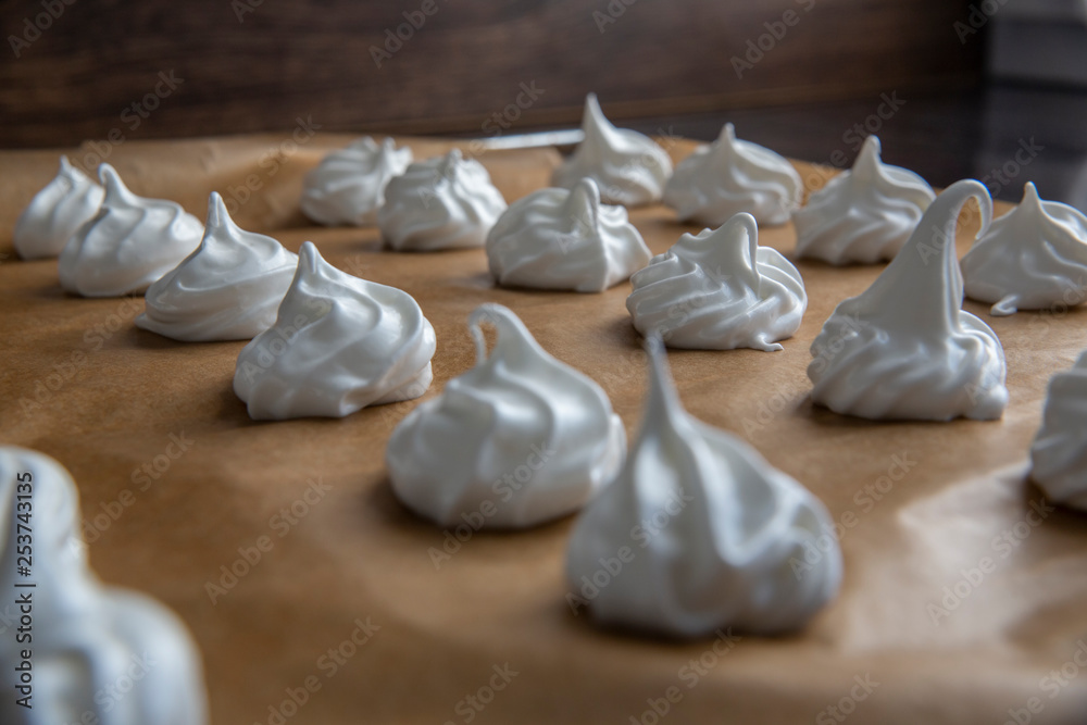 Closeup on raw meringues arranged in rows on brown baking paper