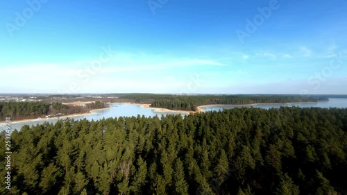 Aerial closing in shot of an enormous frozen lake and spruce forest during winter season, Poland. photo