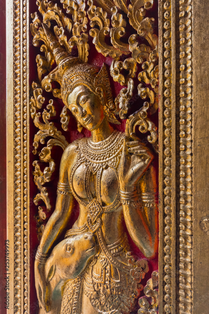 A Buddha on the intricate walls of Wat Xieng Thong in Luang Prabang, Laos.