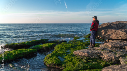 Traveler on a rocky seashore overgrown with green algae