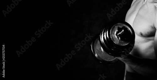 Closeup of a muscular man ready to workout. Part of man's body with metal dumbbell on a dark background