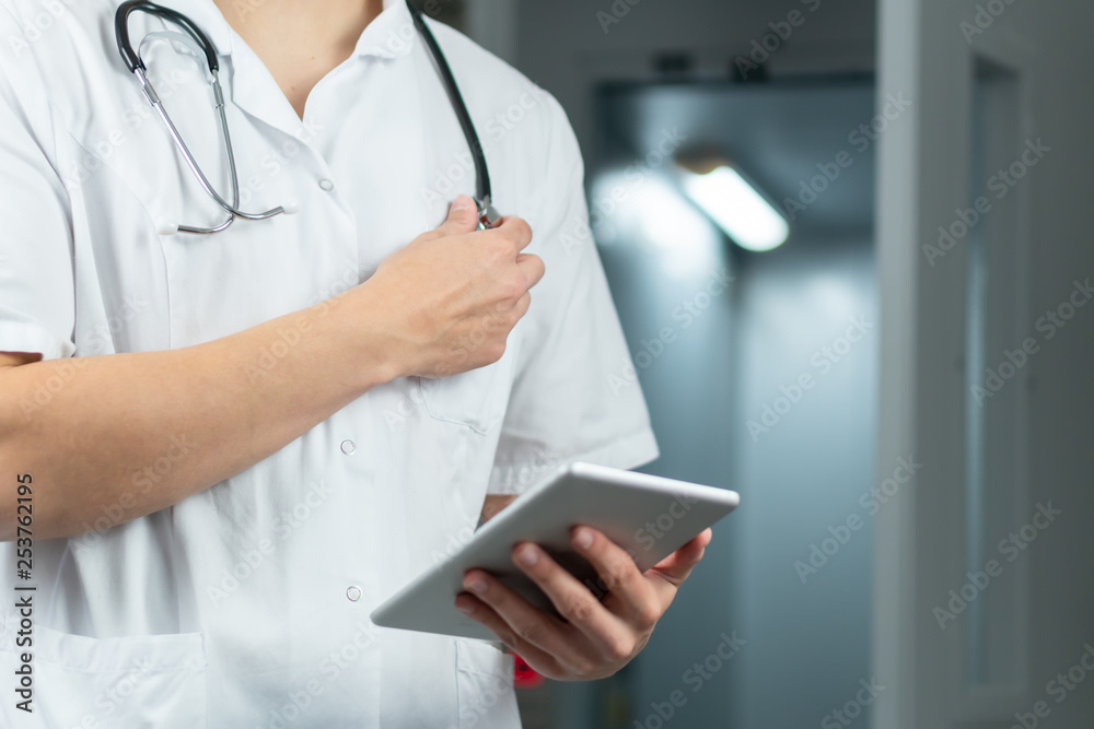 Bright close up of male doctor in uniform holding stethoscope and using computer tablet in hospital. Medical concept with copy space Bright close up of male doctor in uniform holding stethoscope and using computer tablet in hospital. Medical concept with copy space