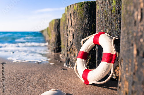 Fototapeta Naklejka Na Ścianę i Meble -  Nostalgic Life Buoy Beach Sea Shore Scene / Vintage red and white miniature life buoy at row of groynes on sandy shore of baltic sea (copy space)