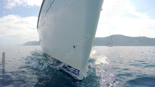 Low angle just over sea surface sailboat bow left to right travelling shot revealing two sailboats sailing to the side