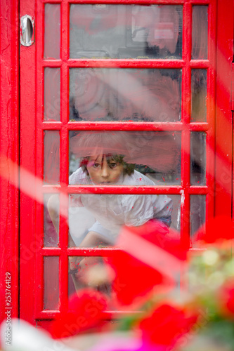 Cute boy, child, calling from a red telephone booth in the city photo