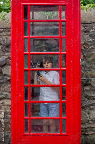 Cute boy, child, calling from a red telephone booth in the city © Tomsickova