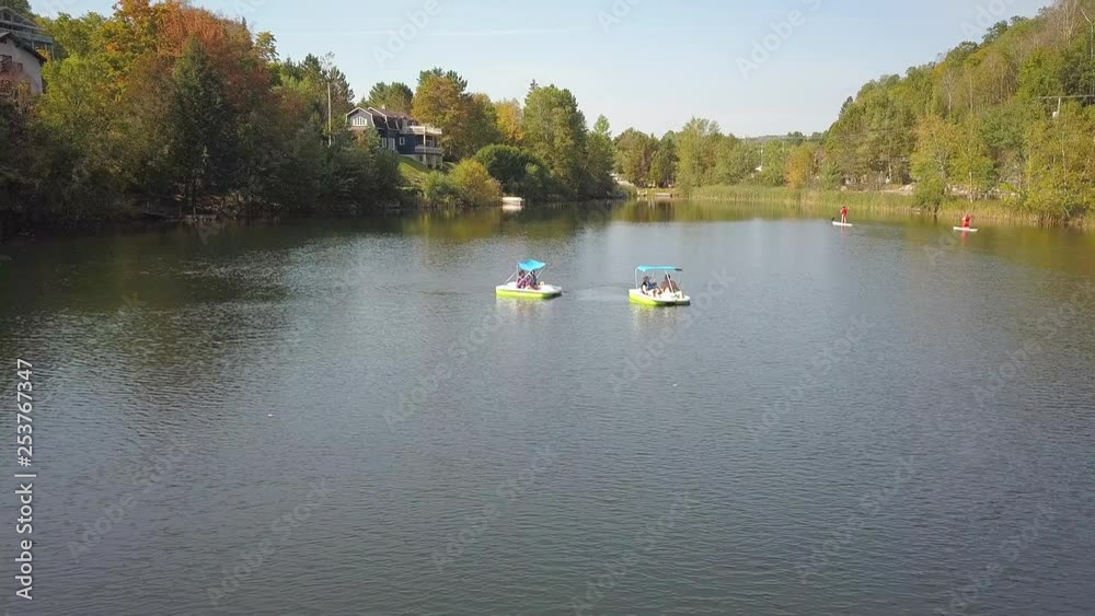 Pedal boats and stand up pads on the lake during summer season with green, yellow and orange trees and mountains on the background. Pedal boats and stand up pads on the lake during summer season with green, yellow and orange trees and mountains on the background.
