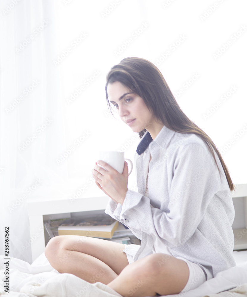 Young beautiful happy brunette woman in black silk dressing gown lying in bed, drinking morning coffee, white cup. Womens day holiday Young beautiful happy brunette woman in black silk dressing gown lying in bed, drinking morning coffee, white cup. Womens day holiday